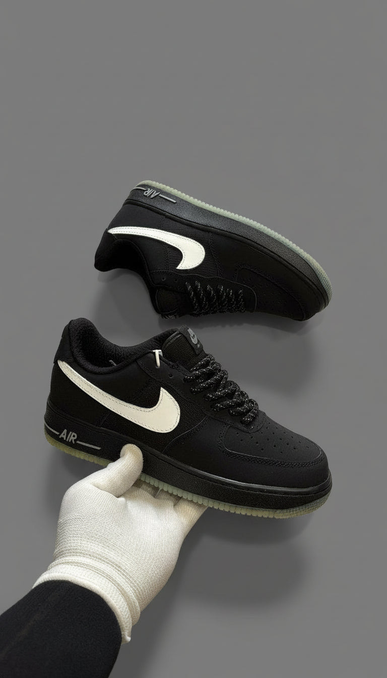Black Nike sneakers with white swoosh logo held by a gloved hand on a stone surface