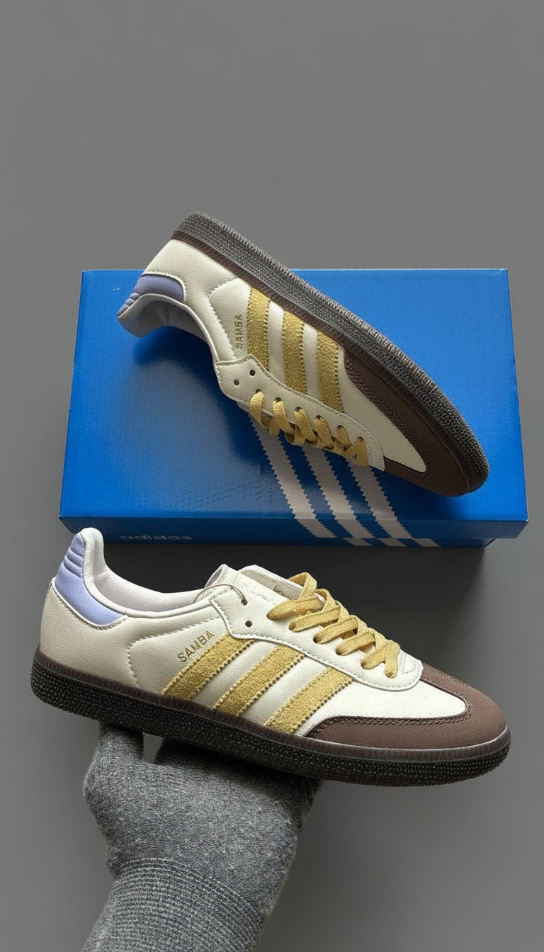 White and brown Adidas sneakers with gold accents on a blue shoe box.