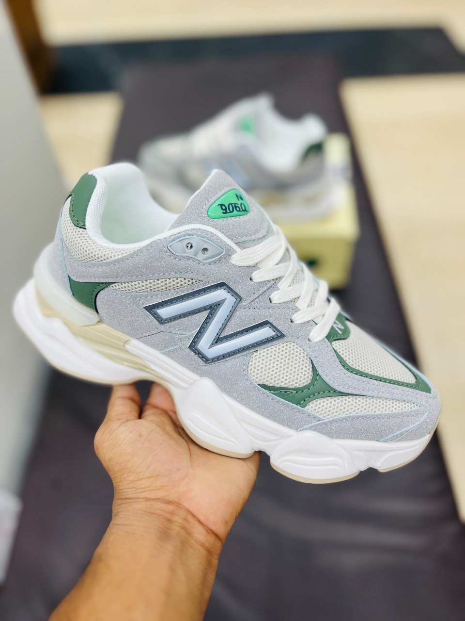 Gray and green sneaker with New Balance logo held by a hand on a dark surface.
