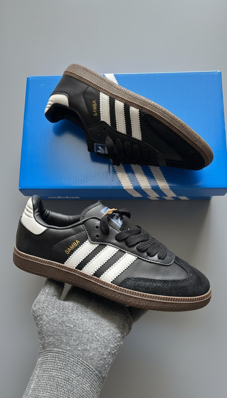 Black Adidas sneakers with white stripes on a blue box and gray surface.