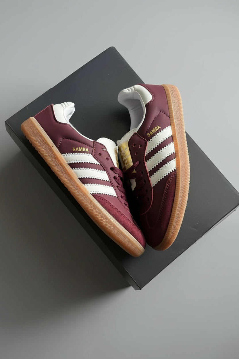 Maroon Adidas sneakers with white stripes on a black box against a gray concrete background