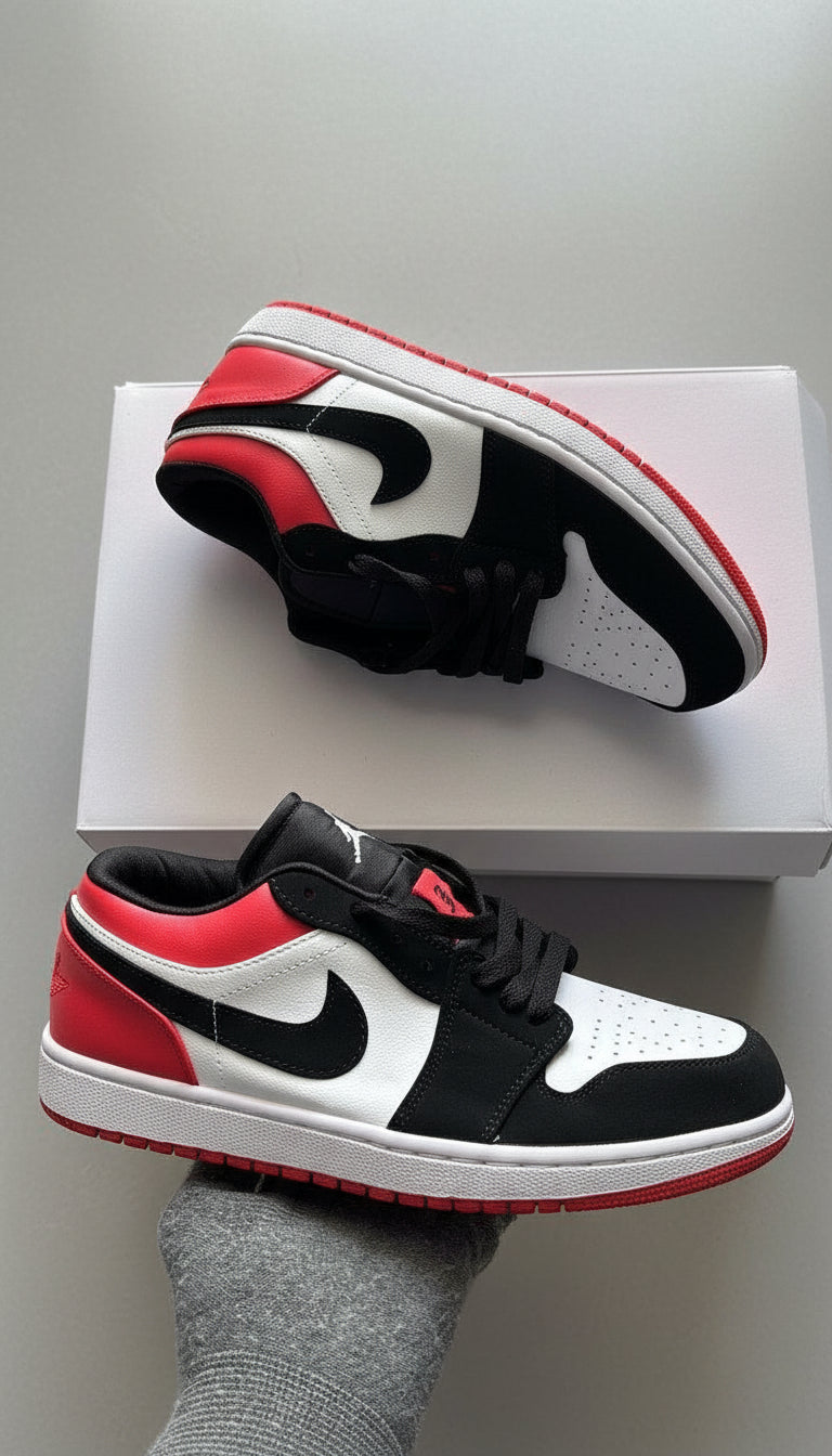 Black, white, and red sneakers on a light gray surface with a white box in the background.