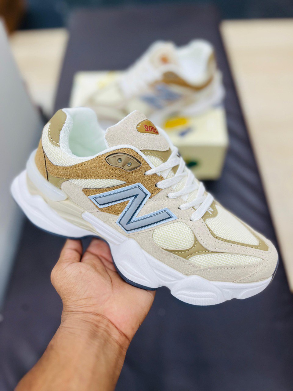Beige and brown sneaker with blue 'N' logo held by a hand, blurred background