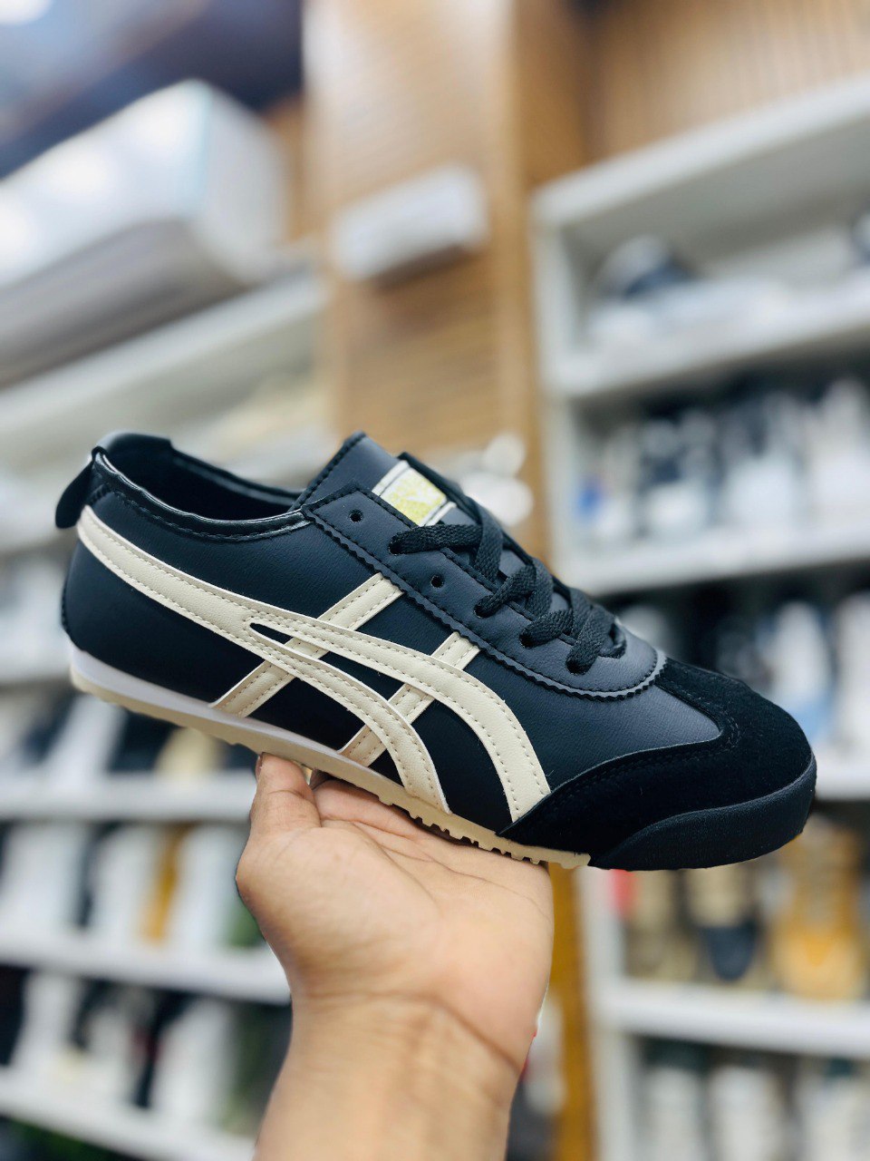 Black and beige sneaker held in a hand with blurred store shelves in the background